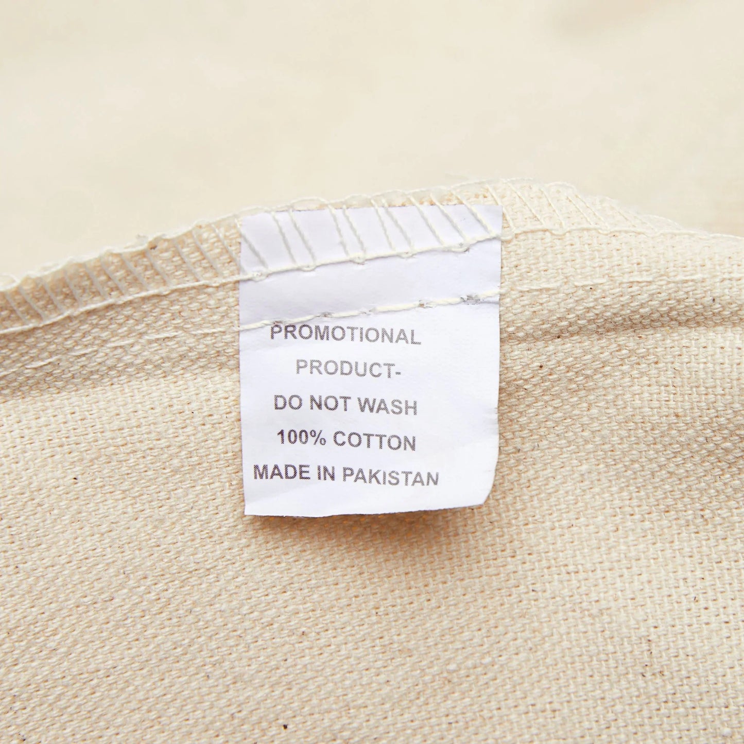 Cotton fabric close-up with sewn tag, showing '100% cotton, do not wash, made in Pakistan'.