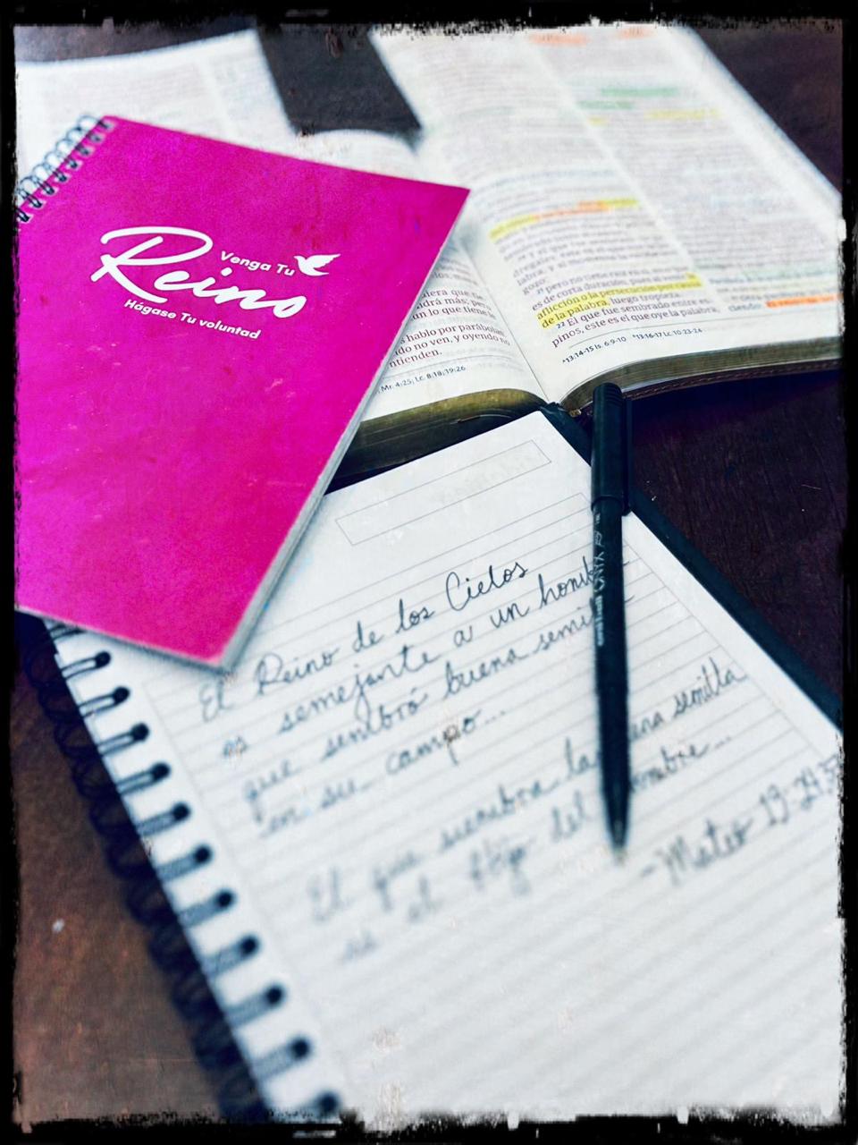 Open Bible, pink Christian notebook, and handwritten notes on a wooden table