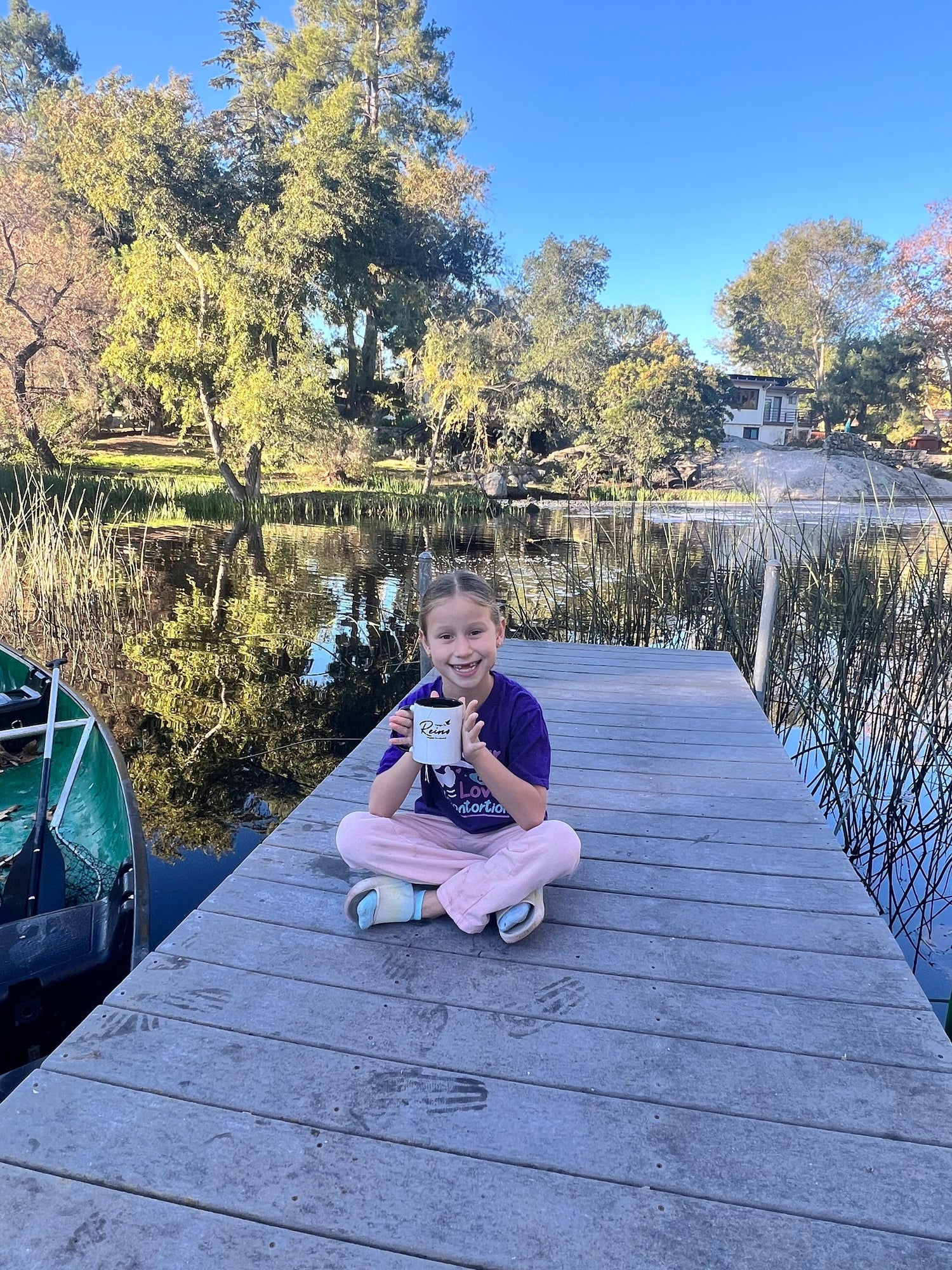 Smiling child on wooden dock by a lake holding a Christian mug, outdoor nature background