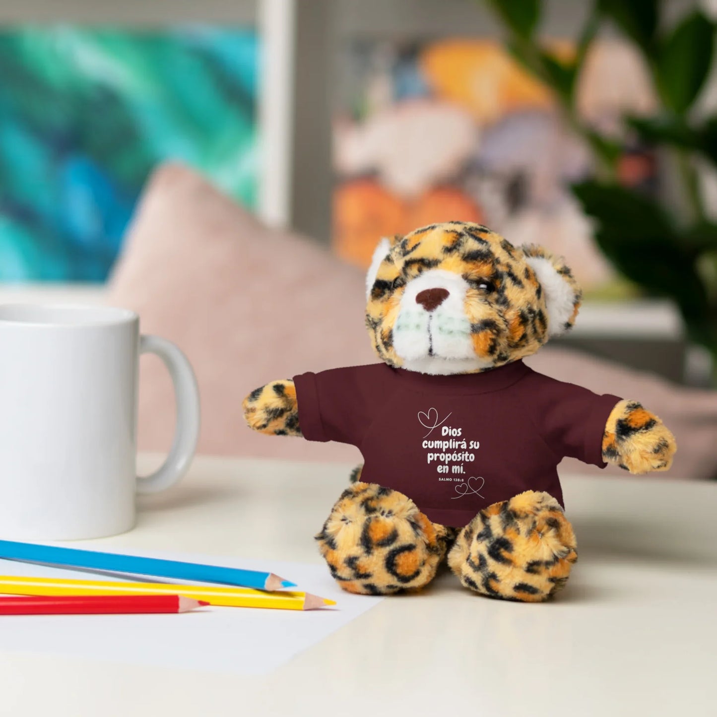 Leopard plush toy with Christian message shirt on desk beside mug and colored pencils
