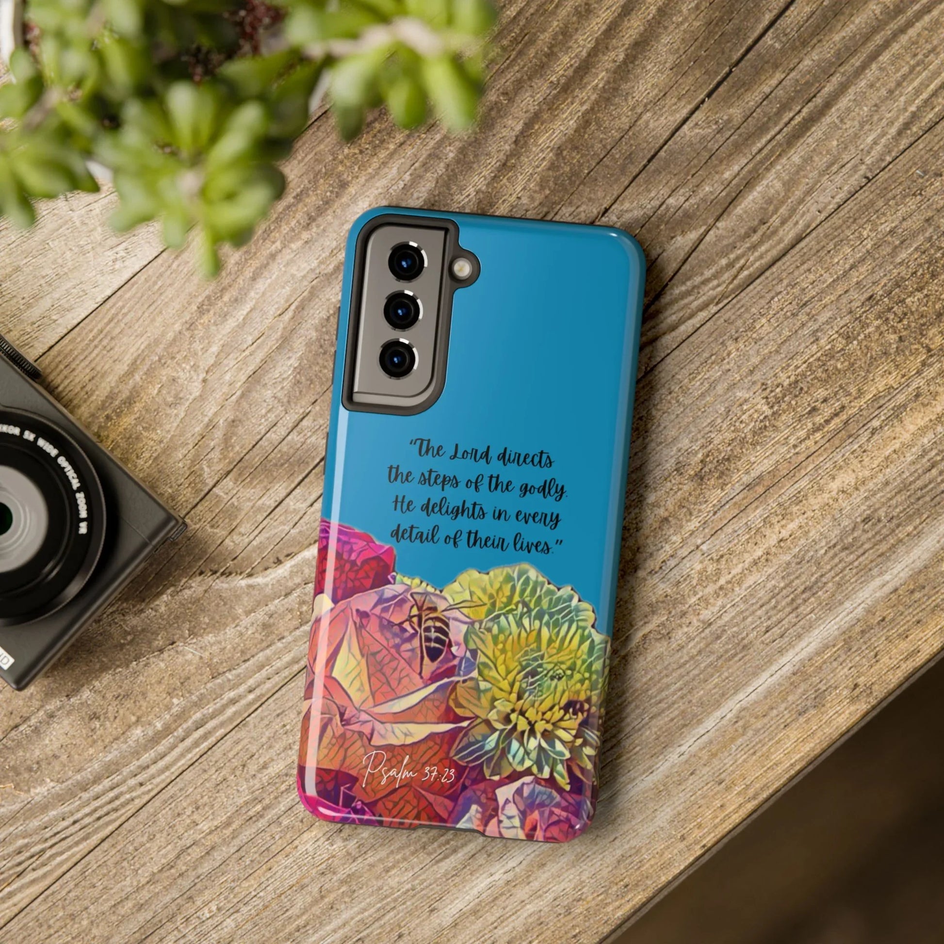 Blue Christian phone case with floral design and Psalm 37:23 Bible verse on wooden table