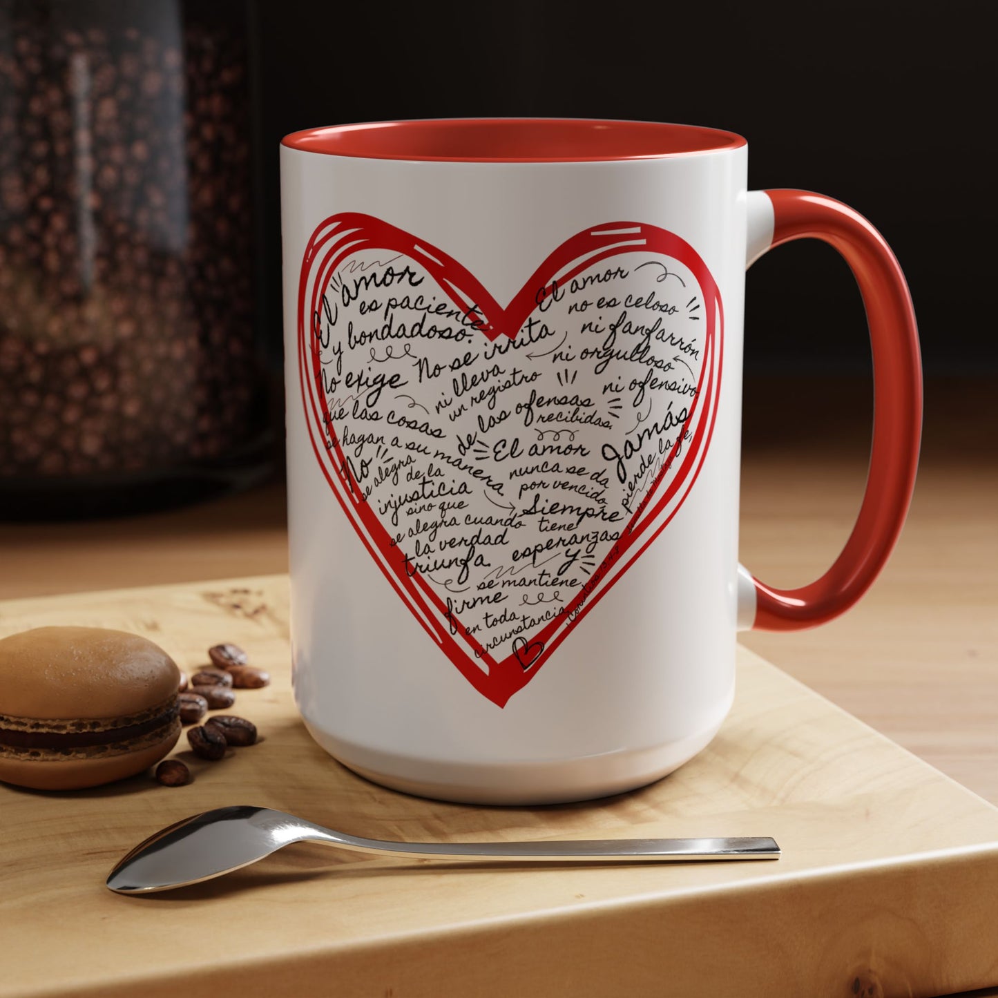 White and red Christian mug with heart and Spanish Bible verse, on wooden table with spoon.