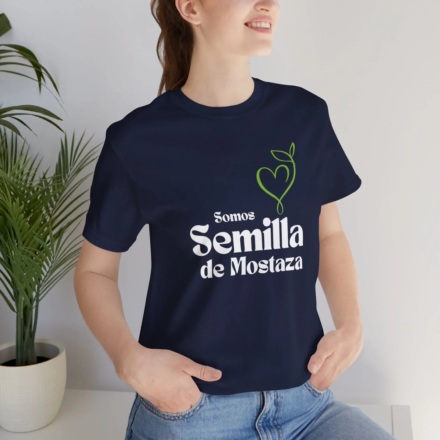 Woman wearing navy Christian t-shirt with 'Somos Semilla de Mostaza' and heart plant graphic.
