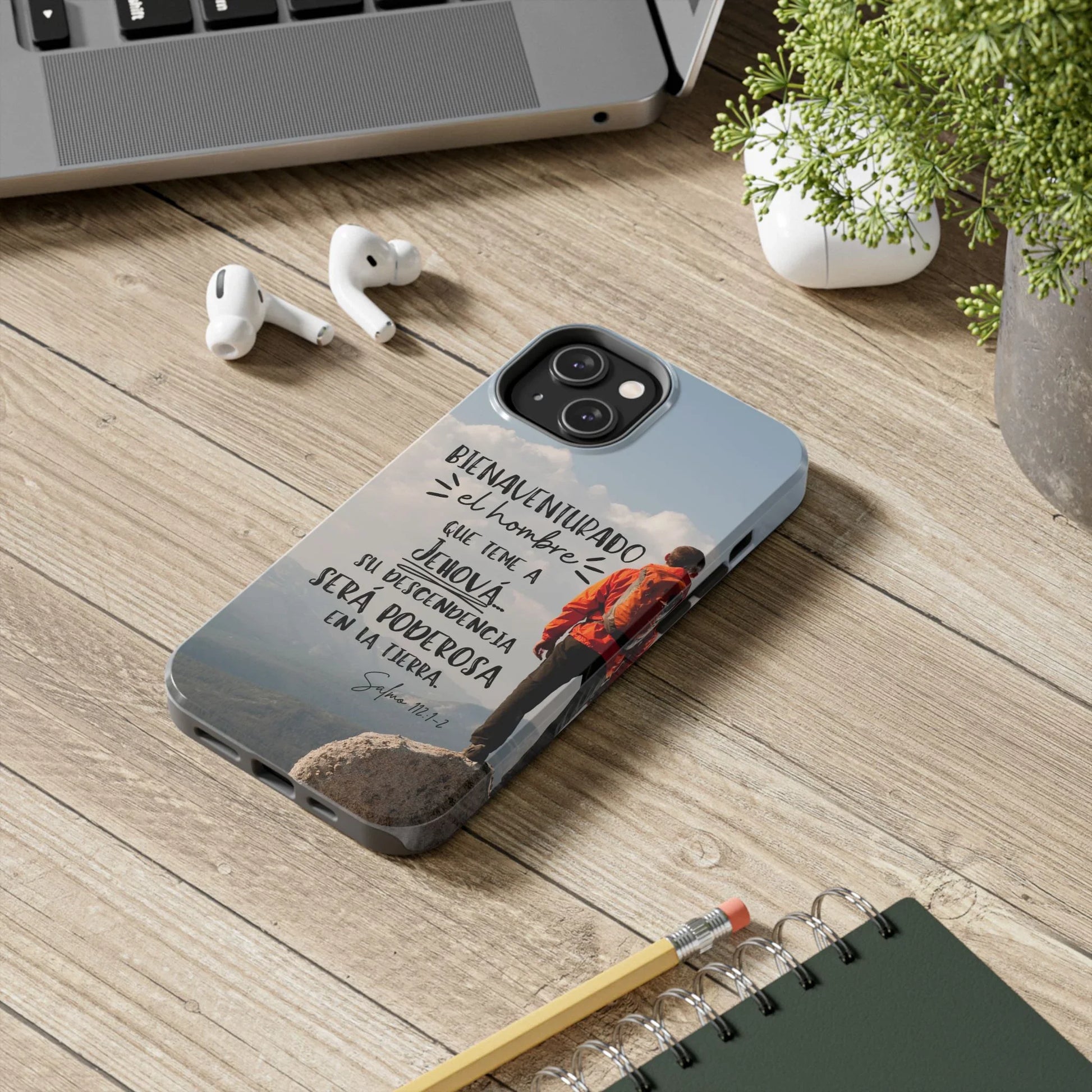 Christian phone case with Spanish Scripture and mountain hiker on wooden desk by laptop