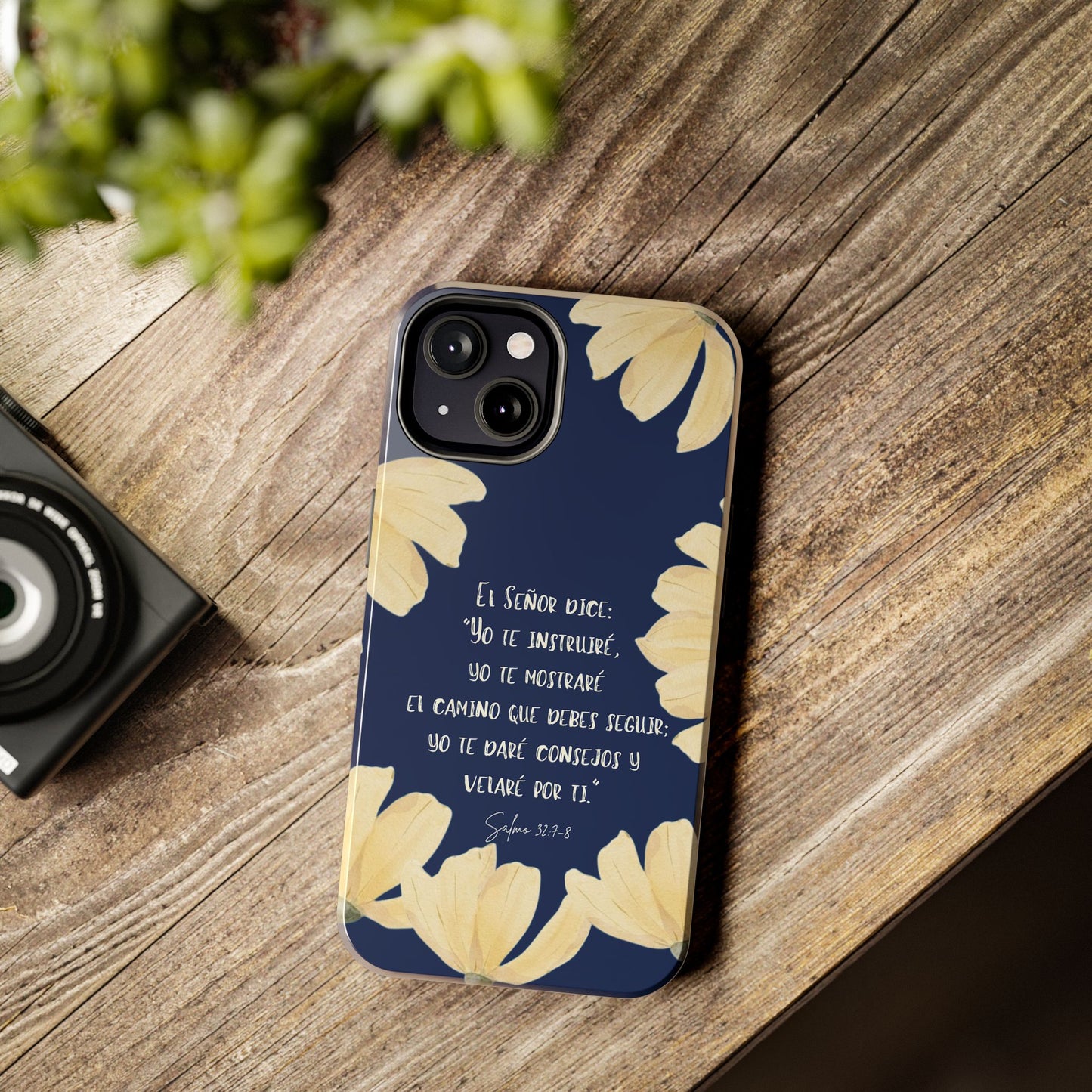Christian phone case with Bible verse in Spanish, navy background, yellow floral design on wood table.