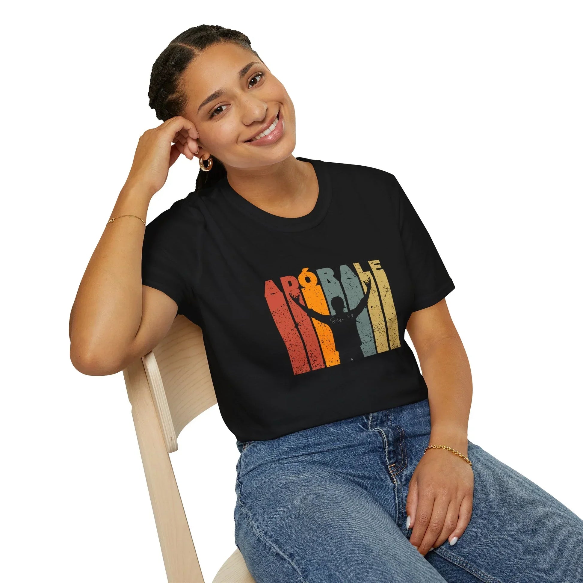 Smiling woman in modern Christian graphic tee with colorful text and worship design, seated on chair.