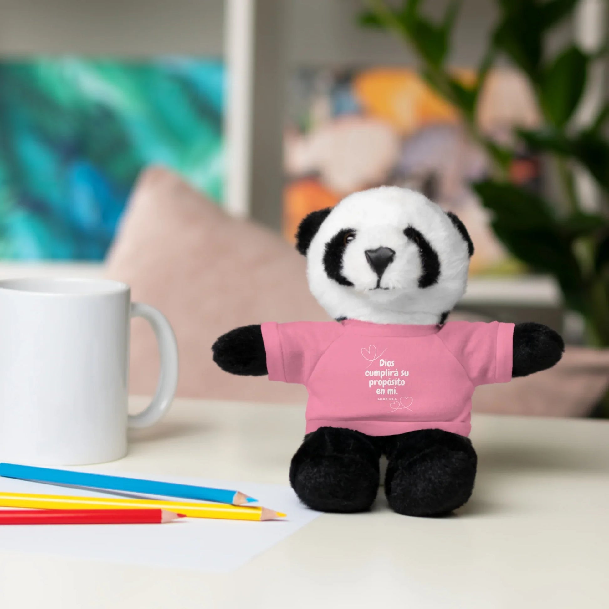 Stuffed panda bear wearing pink Christian message shirt on desk with mug and colored pencils