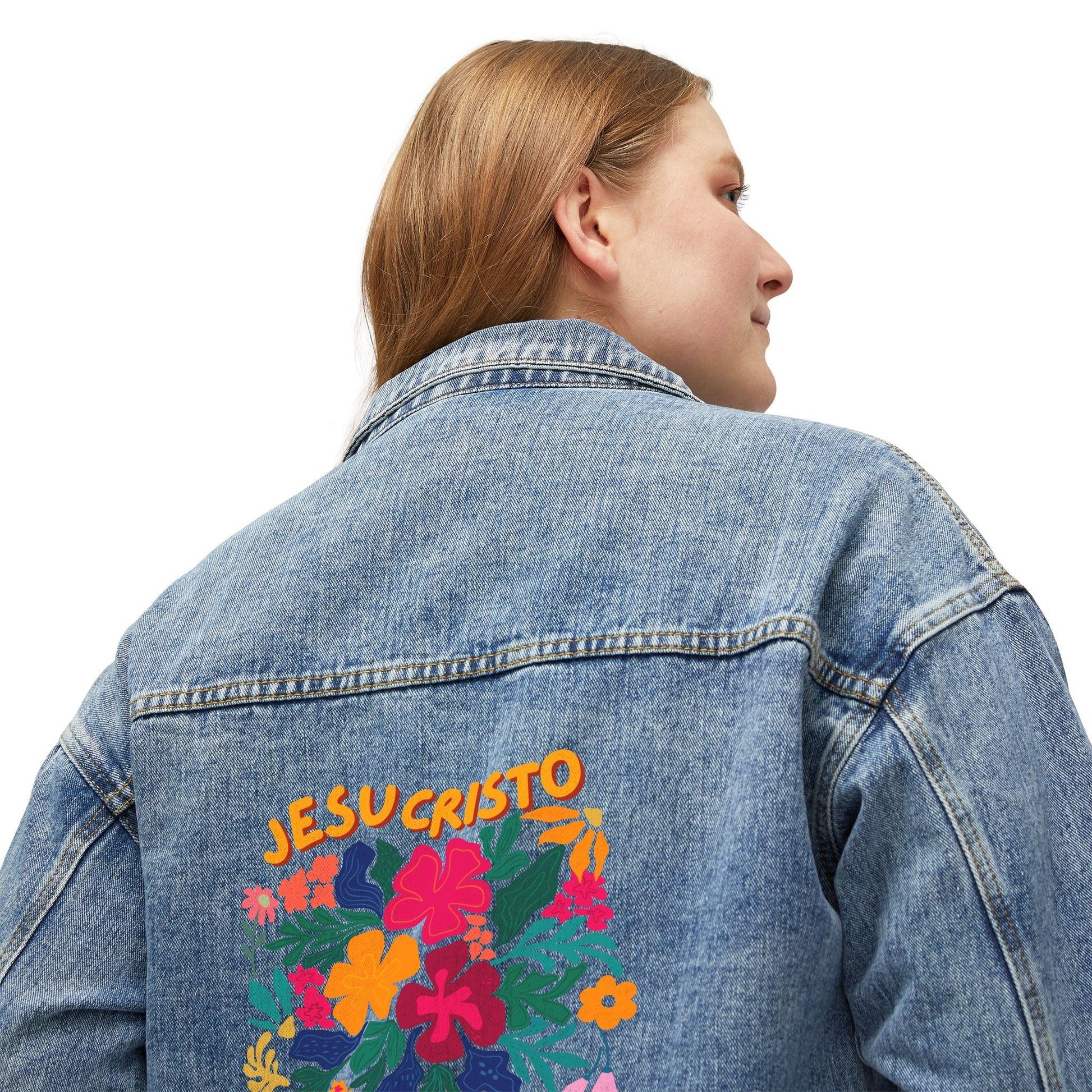 Woman wearing denim jacket with JESUCRISTO and colorful floral Christian design on back