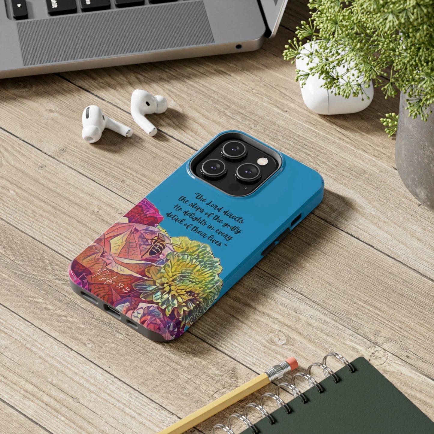 Blue Christian phone case with floral design and Psalm 37:23 Scripture on a desk