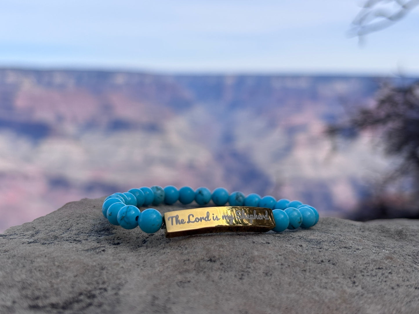 Turquoise beaded Christian bracelet with 'The Lord is my Shepherd' engraved, displayed outdoors.