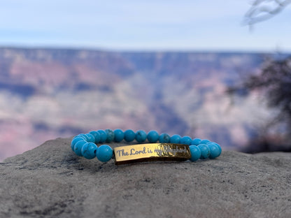Turquoise beaded Christian bracelet with 'The Lord is my Shepherd' engraved, displayed outdoors.