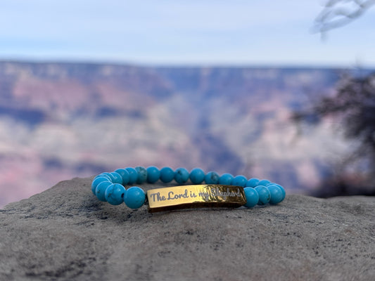 Turquoise beaded Christian bracelet with 'The Lord is my Shepherd' engraved, displayed outdoors.