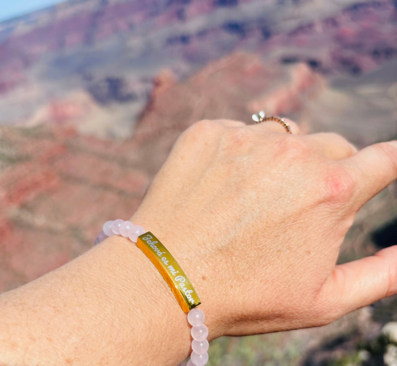 Hand wearing Christian bracelet with 'Jehová es mi Pastor' inscription, outdoors with scenic canyon background