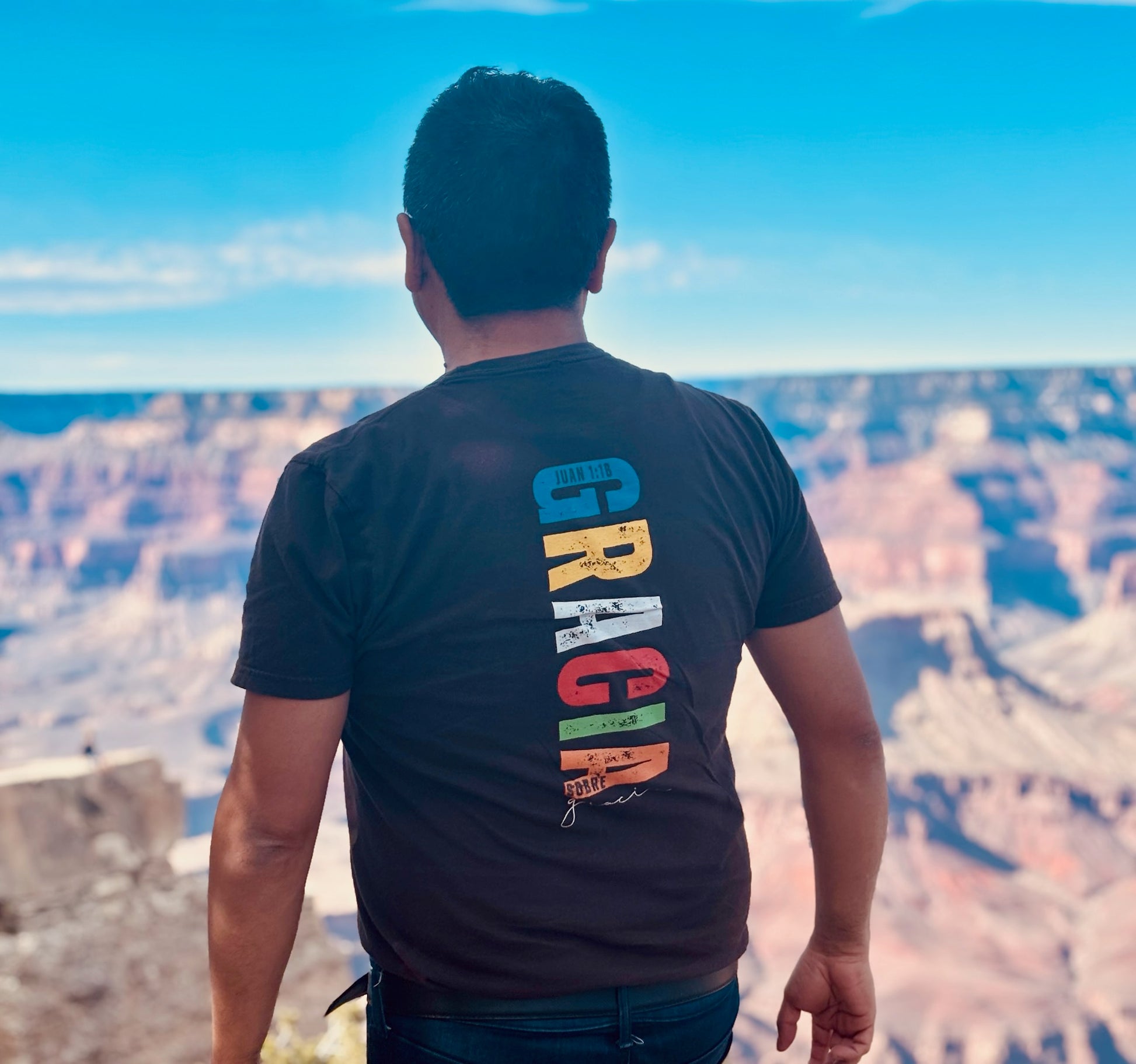 Man wearing Christian graphic t-shirt with colorful text, overlooking canyon landscape