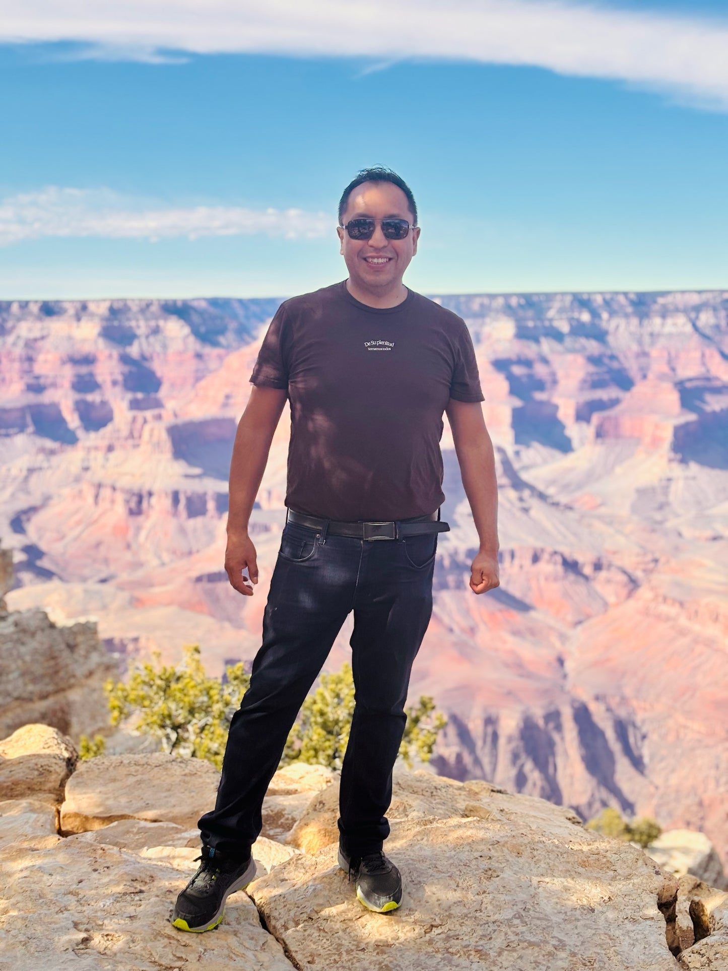 Man in casual outfit and sunglasses standing on rocky edge overlooking the Grand Canyon