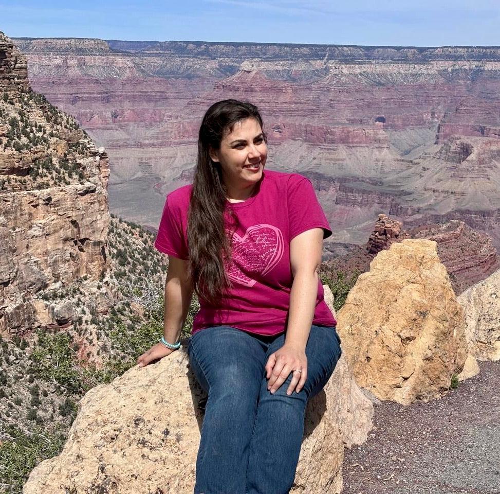 Woman wearing a pink faith-inspired T-shirt sitting on rocks at the Grand Canyon