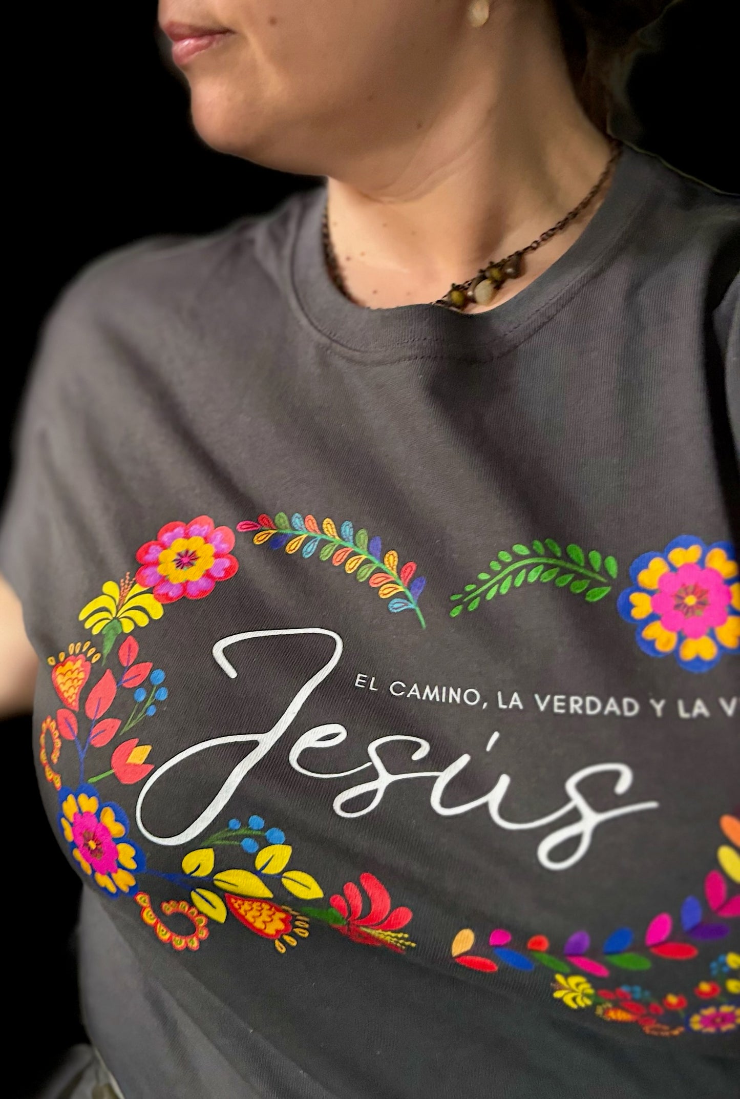 Woman wearing a Christian t-shirt with colorful floral Jesus design and Spanish Scripture text.