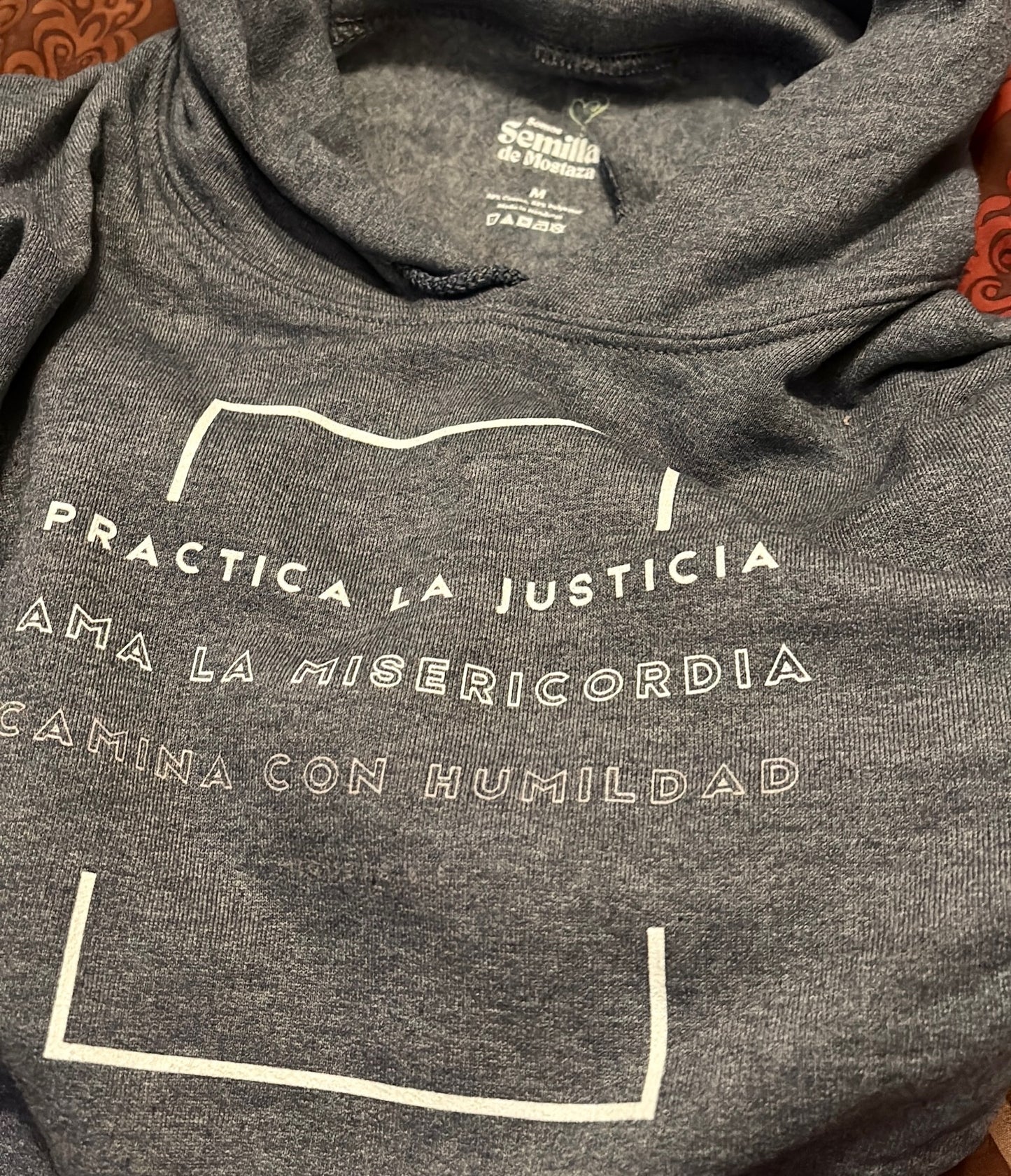 Gray Christian hoodie with Spanish inspirational text 'Practica la justicia, ama la misericordia, camina con humildad' on front.