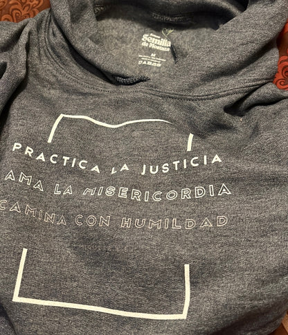 Gray Christian hoodie with Spanish inspirational text 'Practica la justicia, ama la misericordia, camina con humildad' on front.