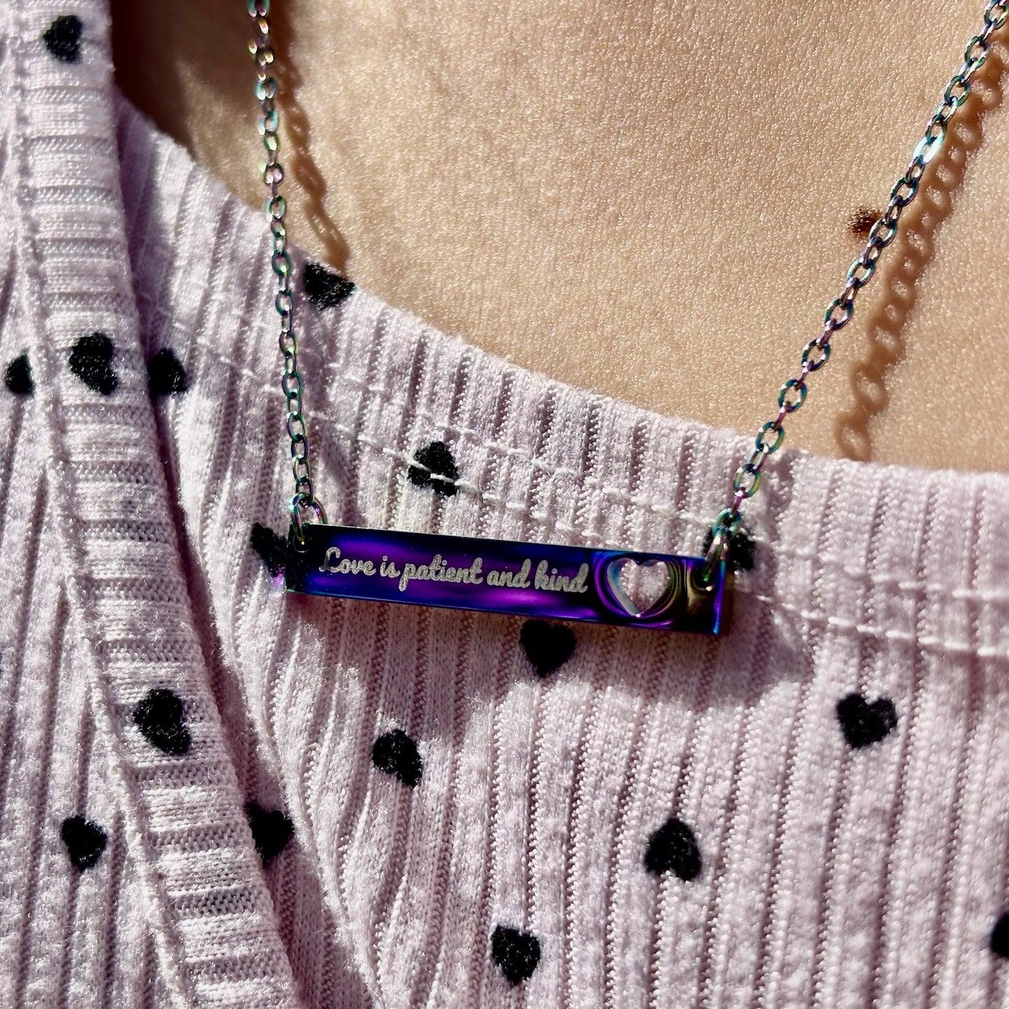 Christian bar necklace with 'Love is patient and kind' engraved, worn over heart print shirt