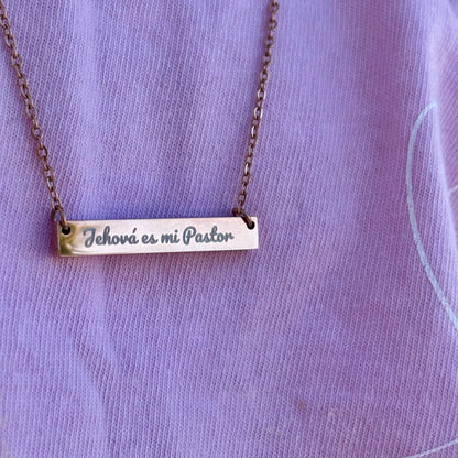 Gold bar necklace with 'Jehová es mi Pastor' engraved, worn on a lavender shirt.