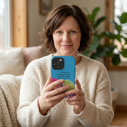 Woman holding a phone with a colorful Christian Scripture case, cozy home setting