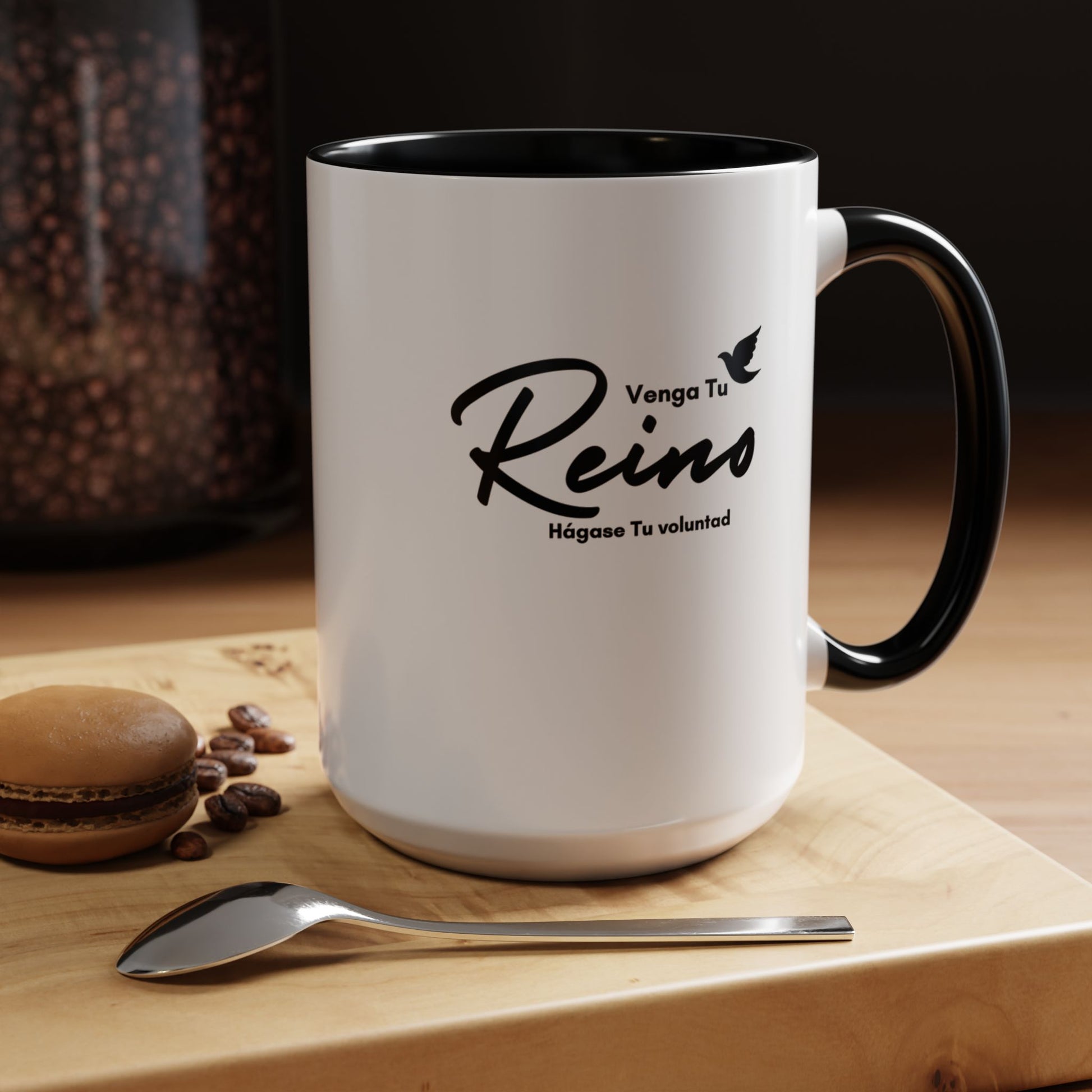 White Christian coffee mug with Spanish Bible verse, next to a spoon and macaron on wooden table