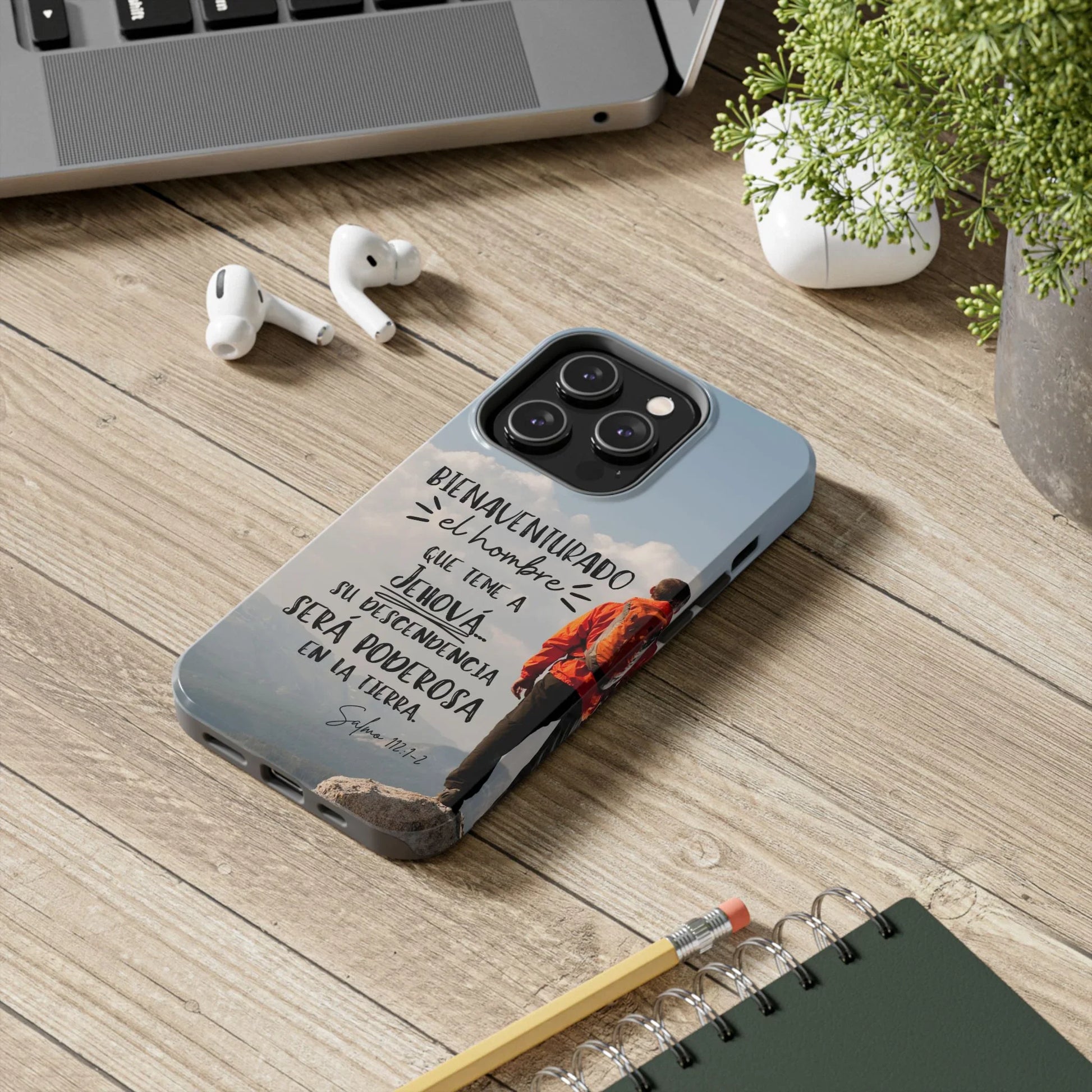 Christian phone case with inspirational Spanish Bible verse, on wood desk beside laptop and notebook