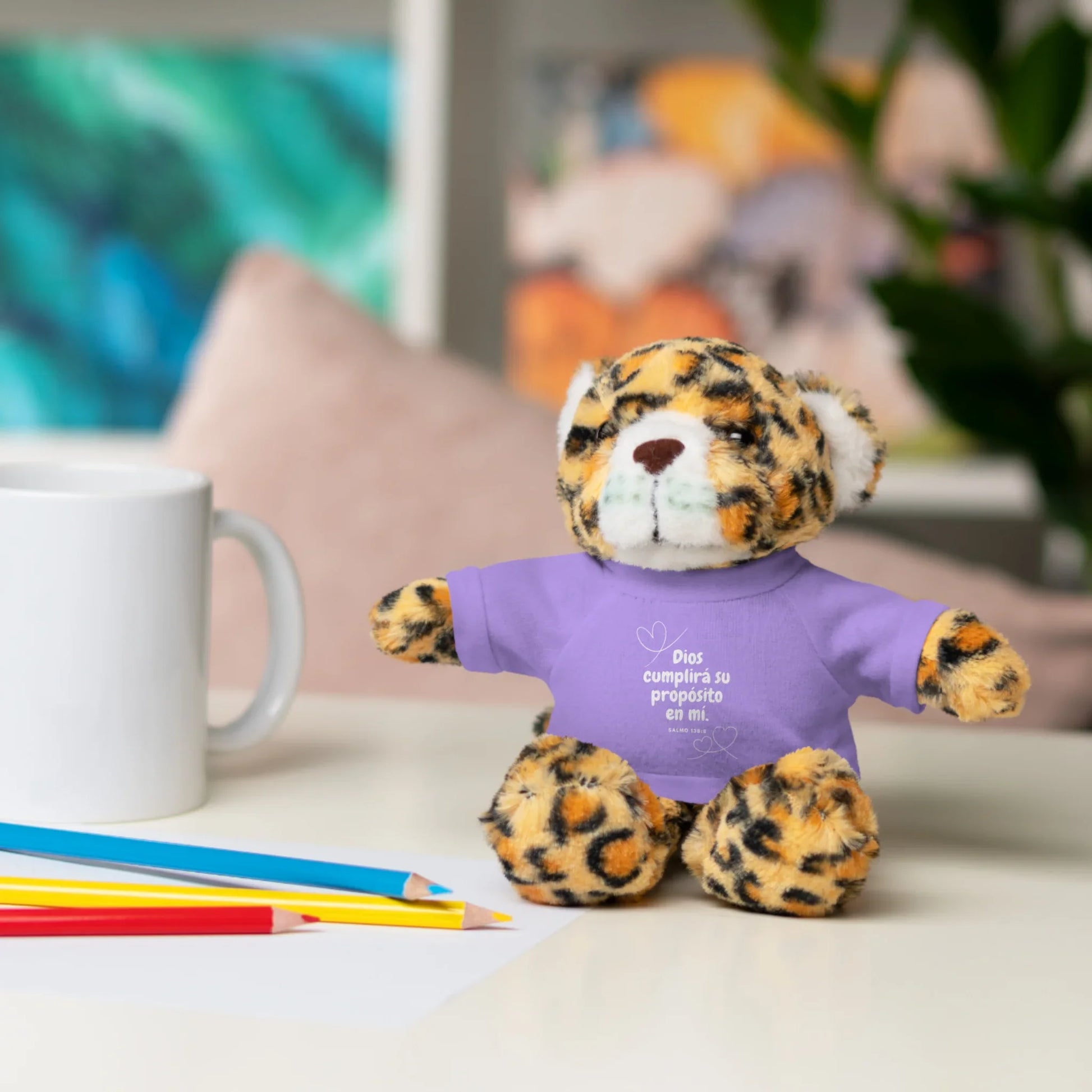Leopard plush toy with Christian message on purple shirt, next to mug and colored pencils.