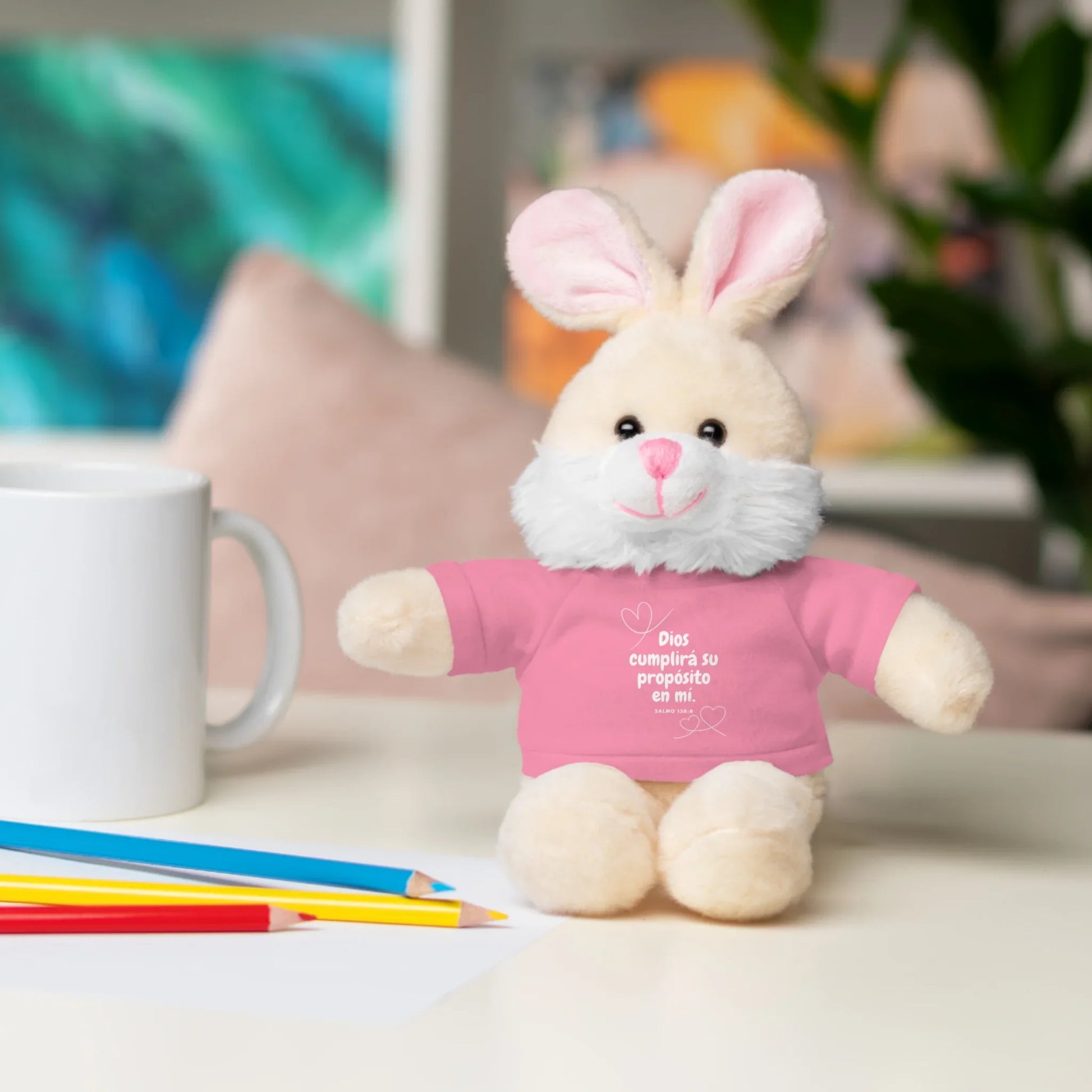Plush bunny with pink Christian message shirt on desk with mug and colored pencils