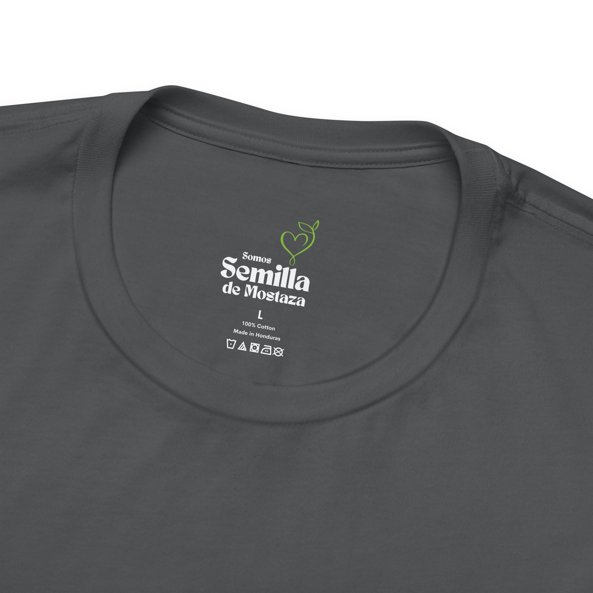 Closeup of dark gray Christian t-shirt label with Semilla de Mostaza text and green sprout graphic