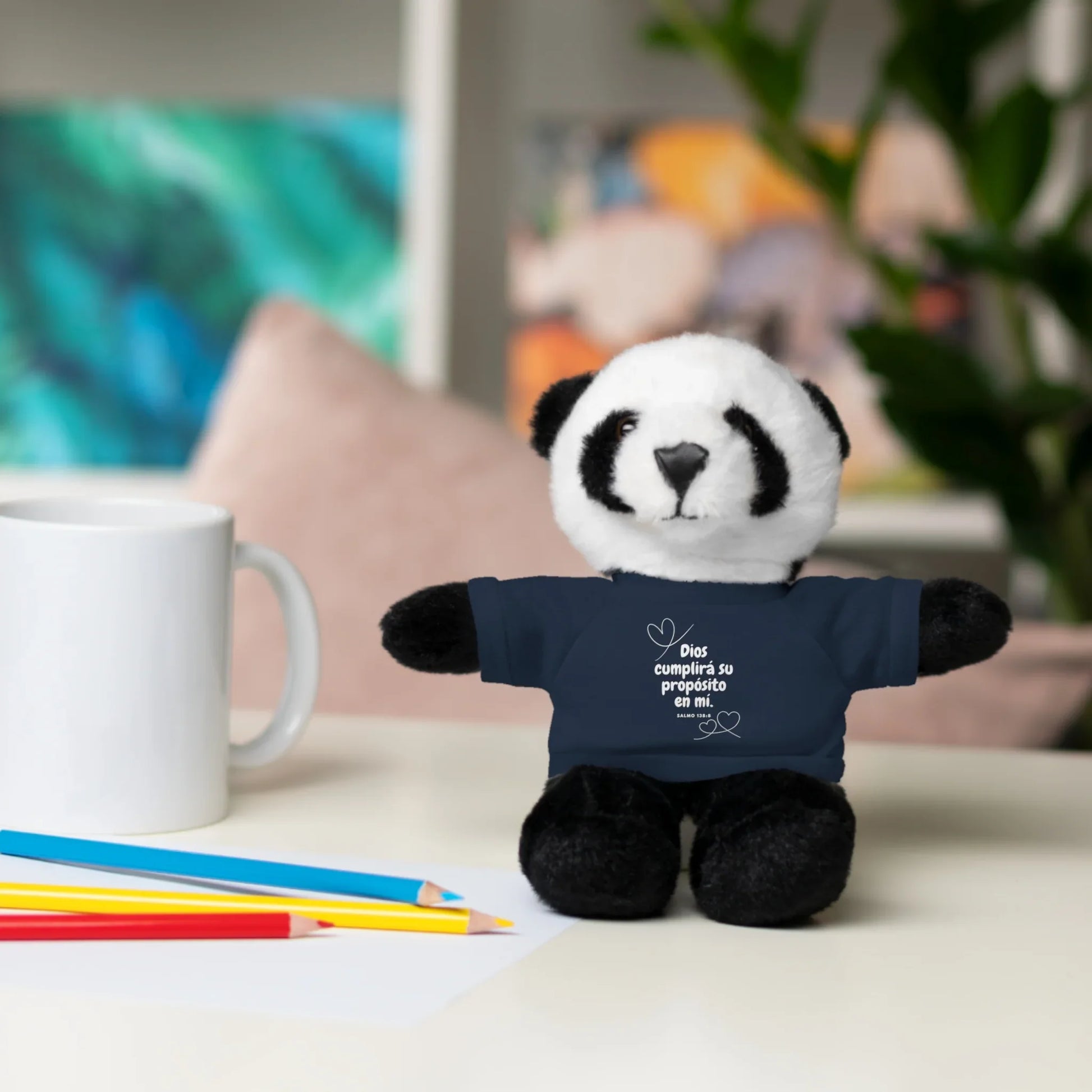 Plush panda toy with Christian Spanish message on shirt, on desk with mug and colored pencils