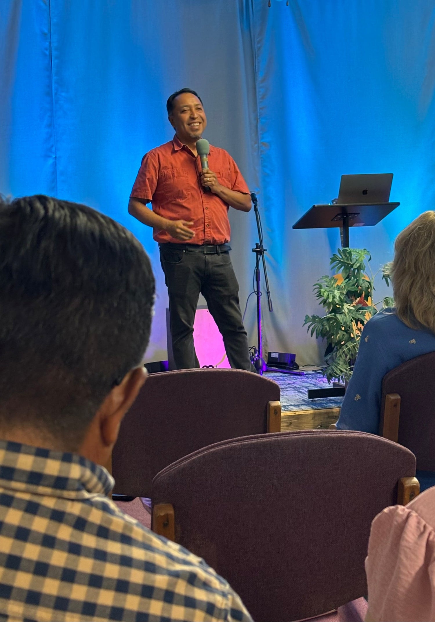 Man speaking into a microphone on a stage at church with an audience